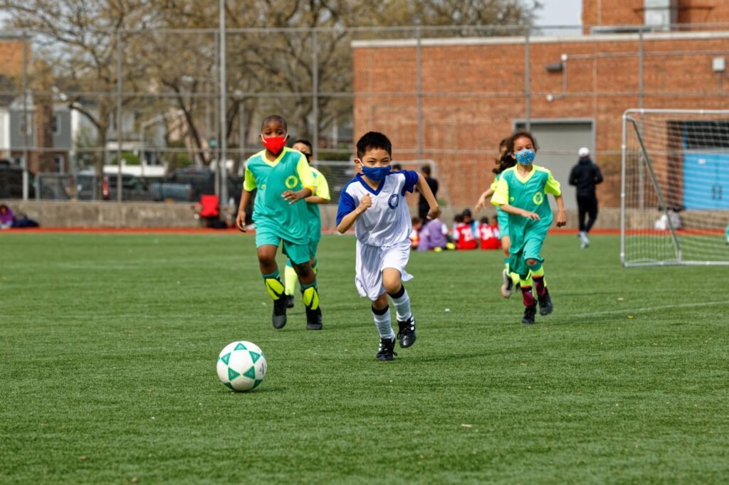 A soccer Player from one of our internal league teams is chasing after the soccer ball as two players from the opposing team follow.